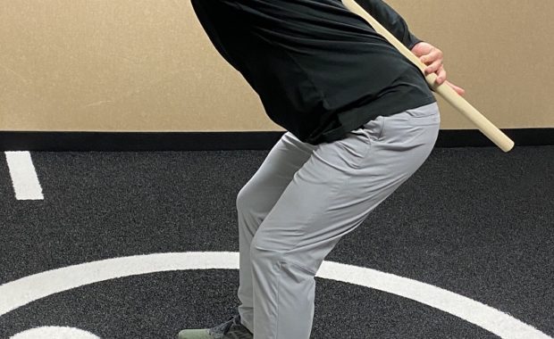 Person holding a dowel across their back while hinging at the hips in the clinic gym